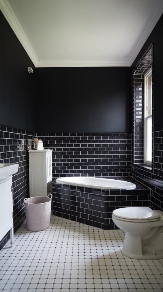 A bathroom with a black accent wall. The wall is tiled with black tiles. The floor is covered with white tiles. There is a white bathtub in the corner. A white cabinet is placed against the black wall. A white basket is placed on the floor. A white toilet is placed against another wall. The ceiling is white. There is a window near the black wall. The room is well-lit.