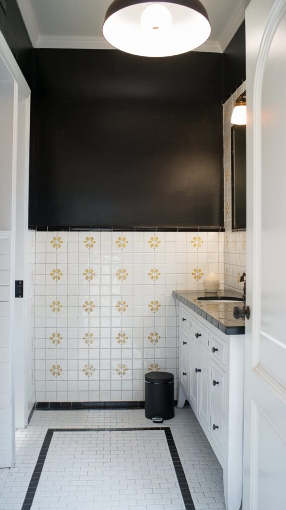 a bathroom with a black accent wall. The wall has a pattern of white tiles with a yellow flower design. There is a white vanity with a black countertop. Above the vanity is a large white light fixture. The floor is tiled in white with a black border. There is a black trash can near the wall. The room has a white door.