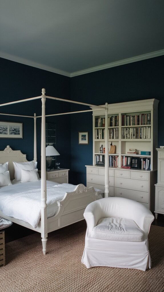 A cozy cottage-style dark blue bedroom with white furniture, including a four-poster bed, an armchair, and a built in bookshelf.