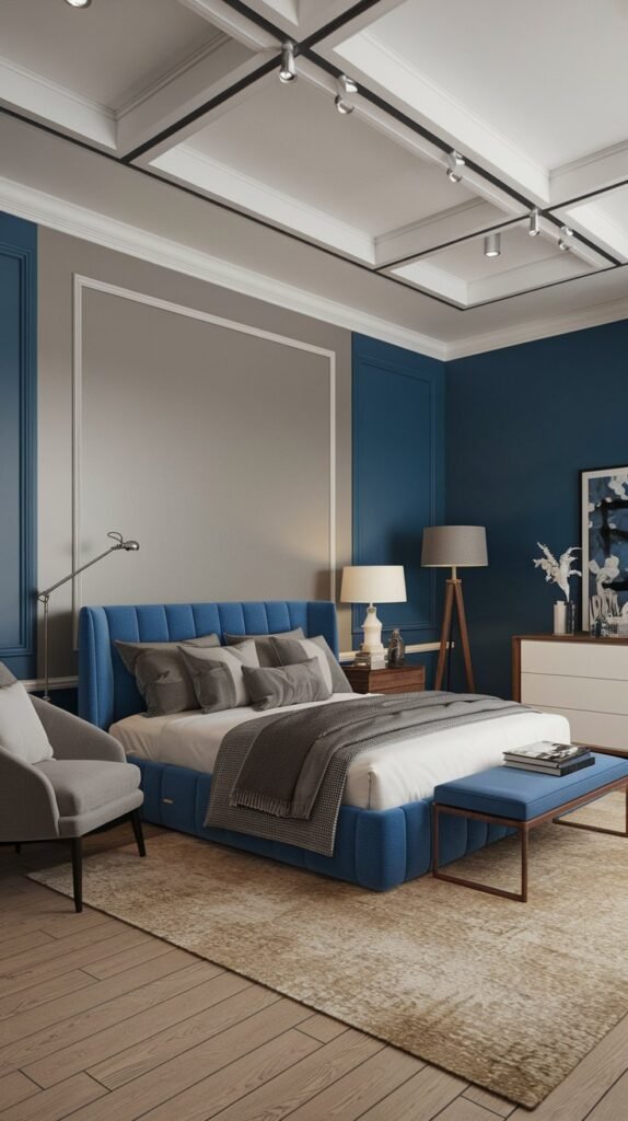 A modern bedroom with a blue accent wall, gray walls, a blue bed, gray bedding, and a gray chair, and light colored hardwood floor.
