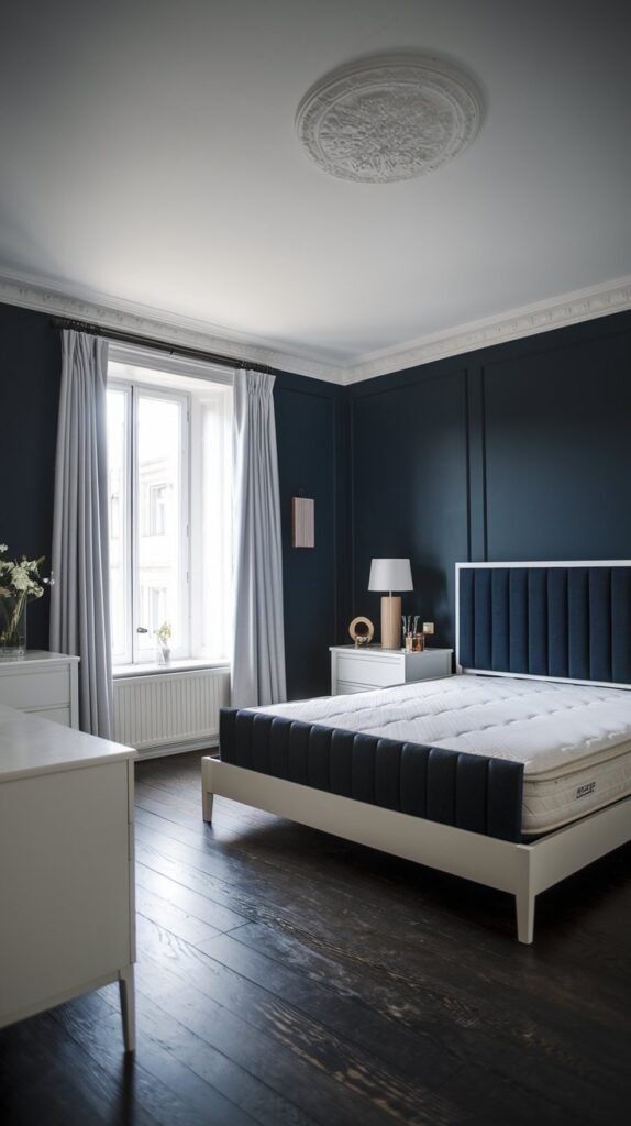 A bedroom combining modern and classic elements, with panelled walls, white trim, a tufted headboard, light-colored curtains, and dark hardwood floors.