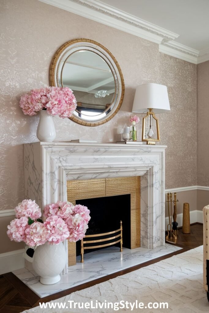 A marble fireplace decorated with pink hydrangeas and a round mirror.