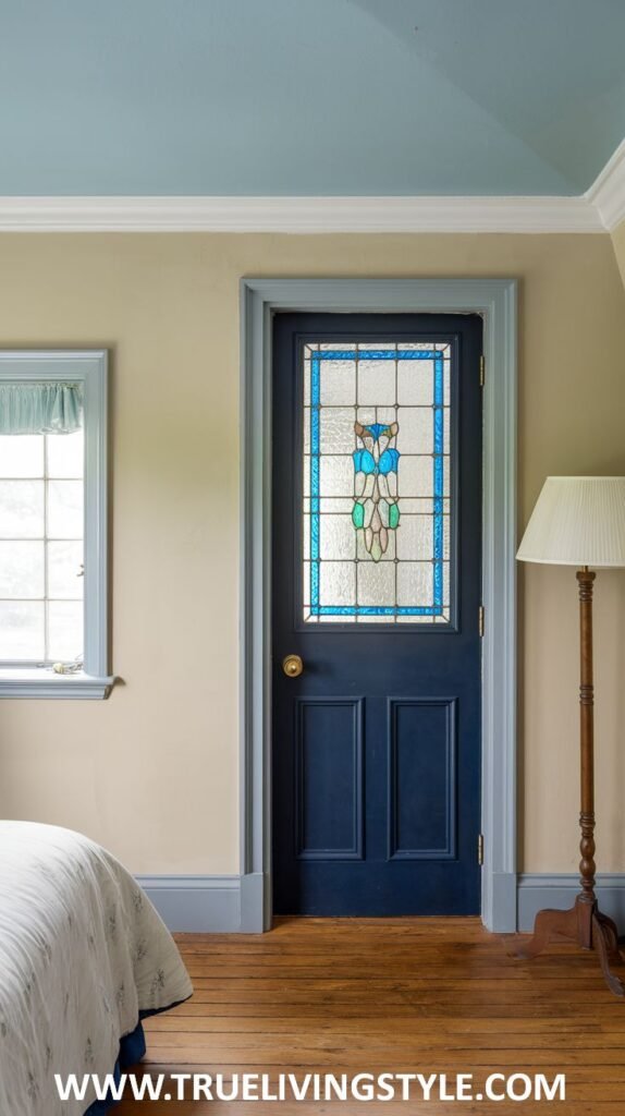 A charming bedroom with cream walls and a light blue ceiling. A dark blue door with stained glass is a focal point. A bed with light-colored bedding is partially visible.