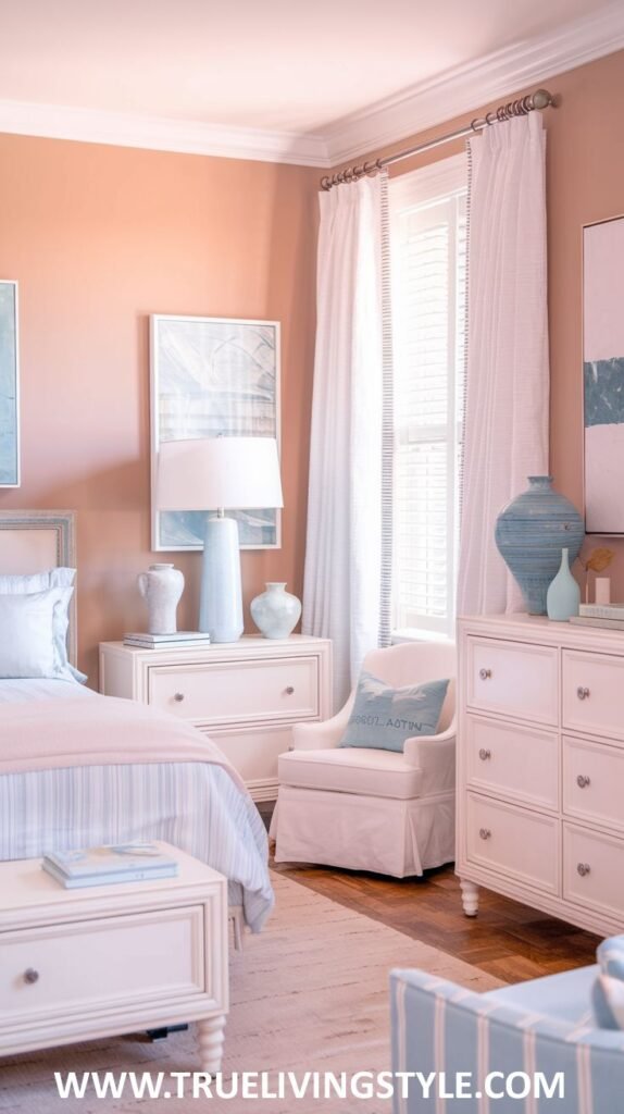 A calming bedroom with soft peach walls and white furniture. A bed with white and light pink bedding is shown, along with a white armchair with a blue pillow.