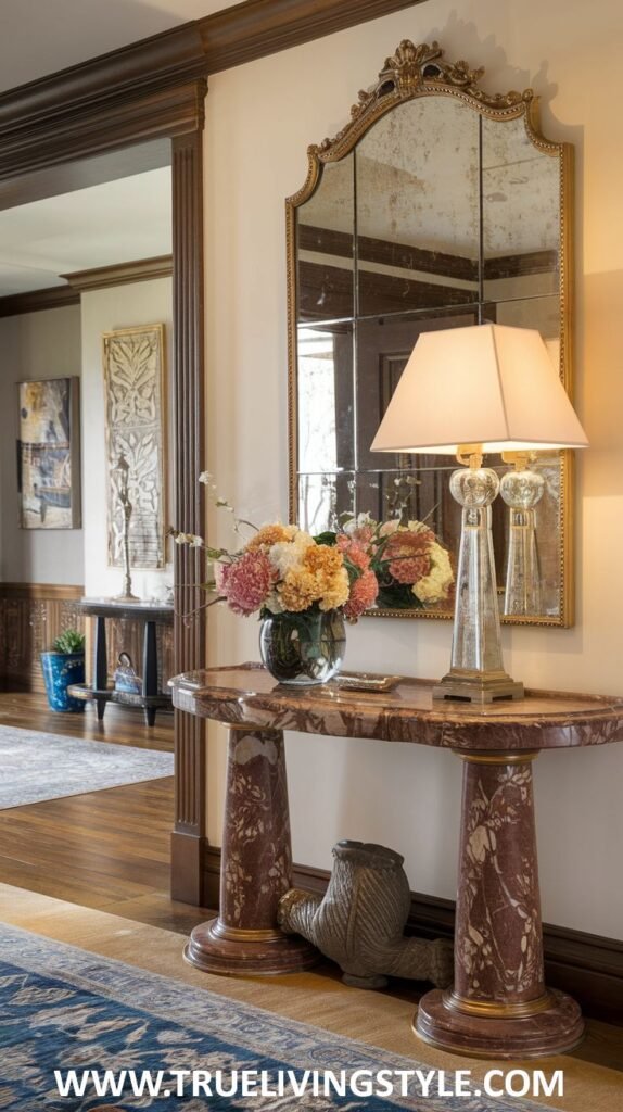 A marble-topped console table with a vase of flowers and a crystal lamp is set against a wall featuring a large, ornate multi-paneled mirror.