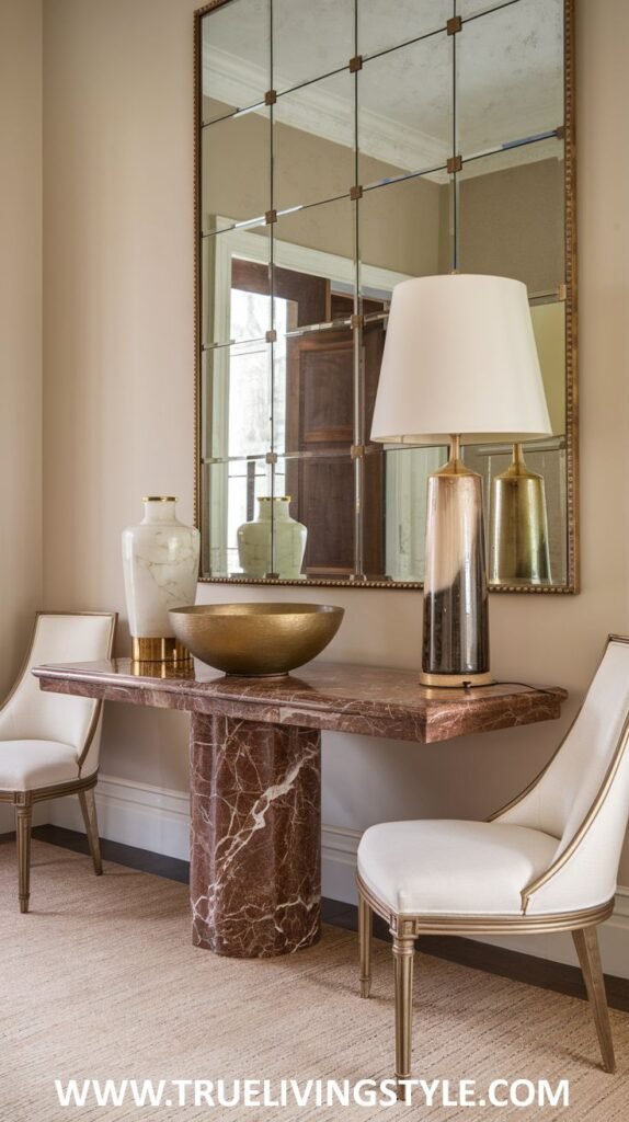A marble console table holds two vases, a gold bowl, and a lamp, flanked by two chairs and placed in front of a large multi-paneled mirror.