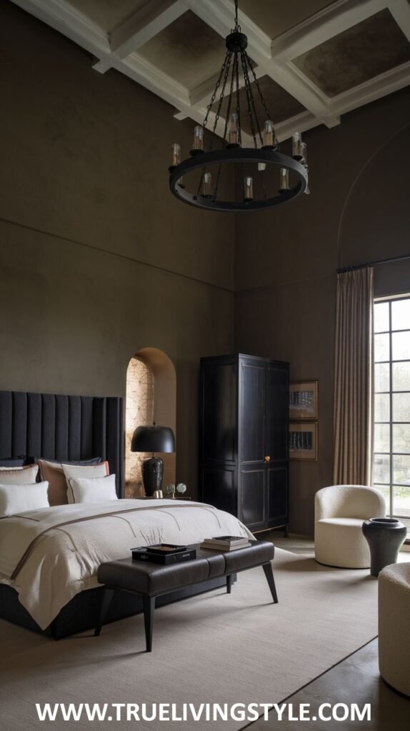 A dark earthy bedroom with dark brown walls and a coffered ceiling contains a bed with a tall black headboard and light bedding, a dark leather bench, a black wardrobe, a round glass table, and a light beige armchair.