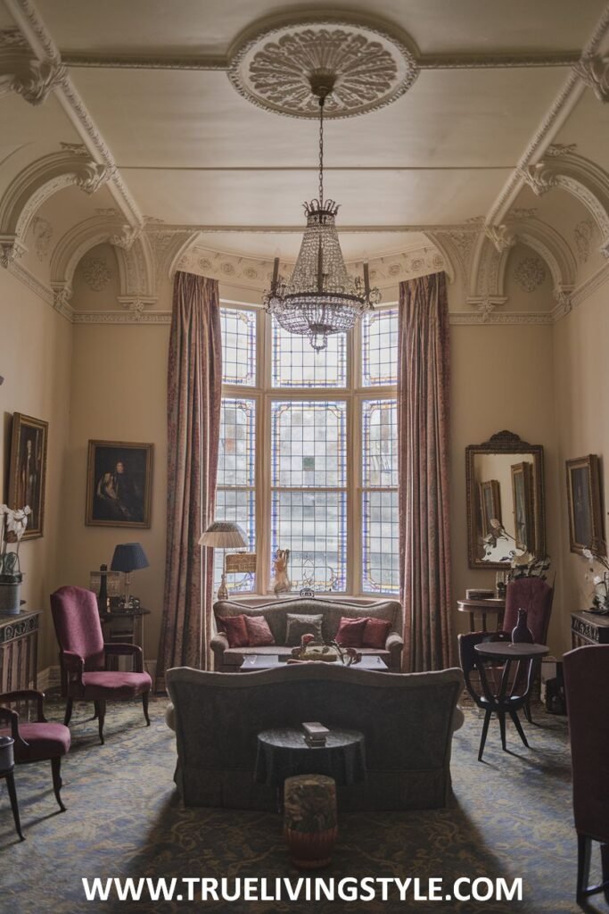 A beautiful stained glass window is a unique architectural highlight in this luxury Victorian living room. The room is comfortably furnished and features a crystal chandelier, blending character with Victorian luxury in the living room.