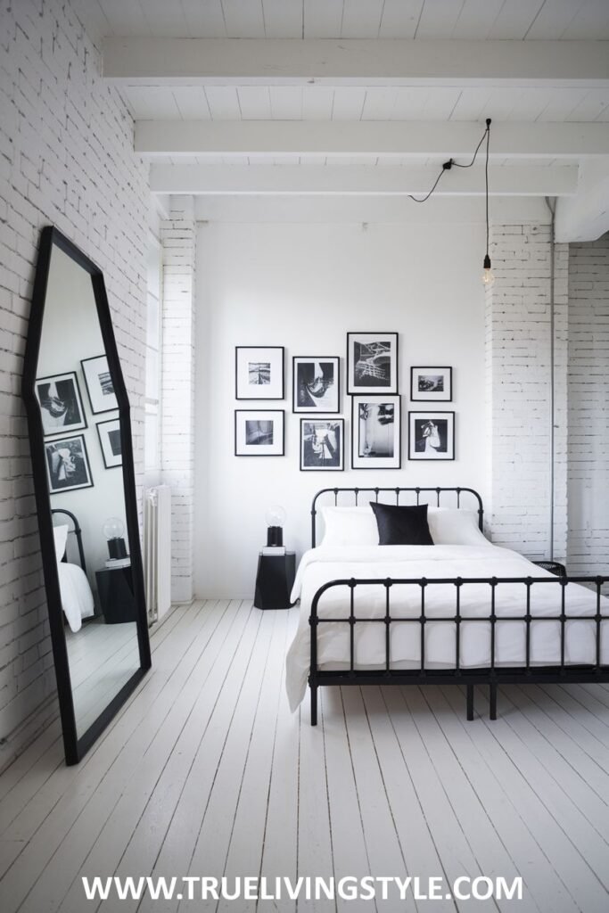 A collage of black-and-white photos hangs on the wall in a bedroom with a black metal bed frame.