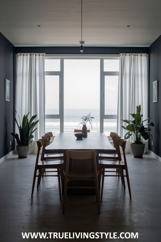 A dramatic dark minimalist dining room with dark walls, a long wooden table, simple wooden chairs, and large windows.