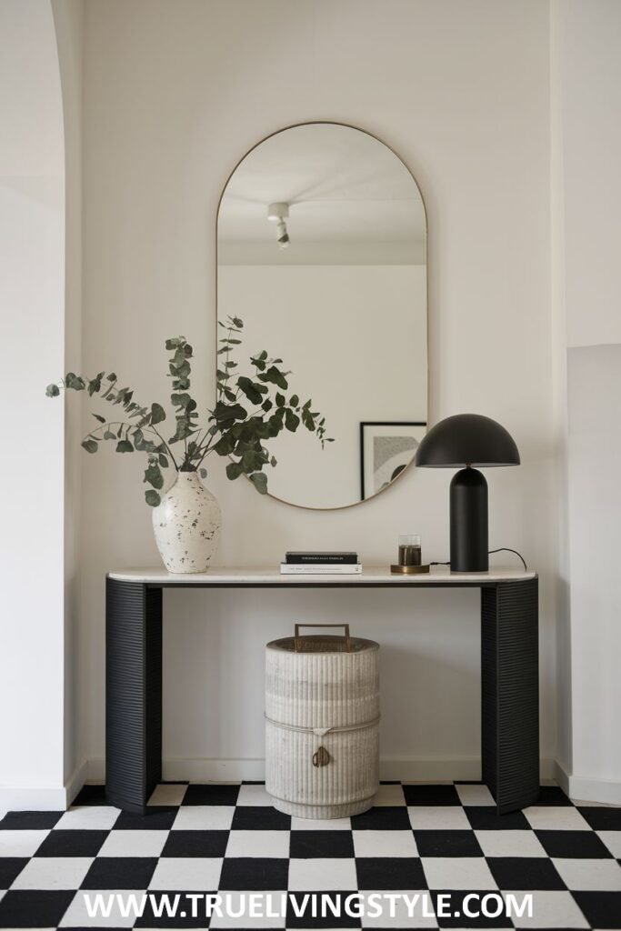 An entryway with a round mirror above a console table, a lamp, a vase, and a basket, set against a black and white checkered floor.