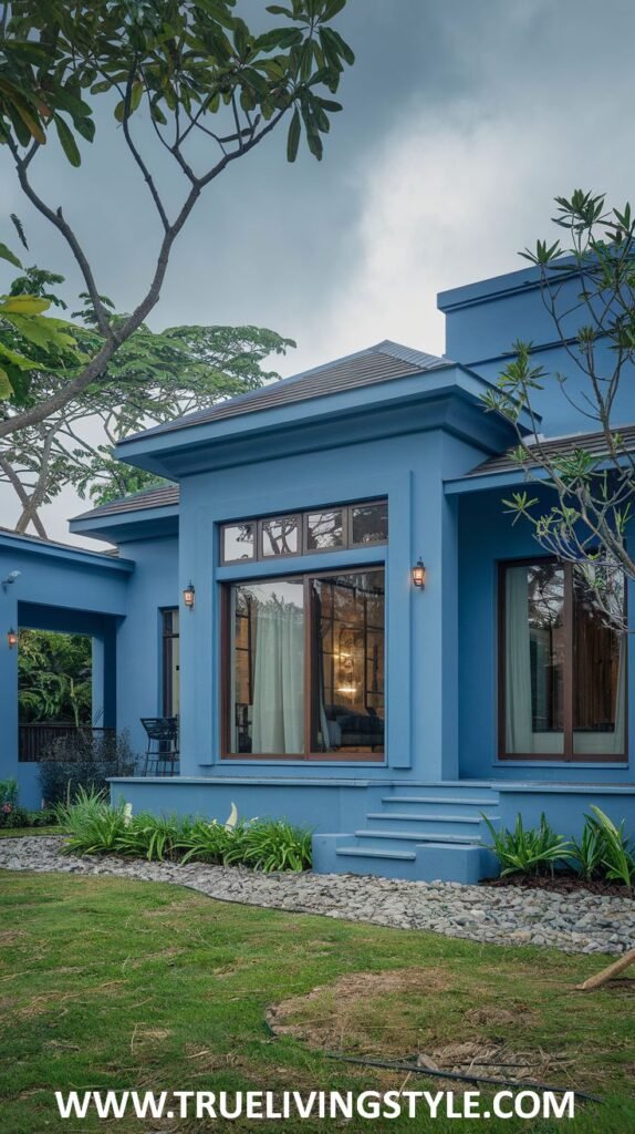 A low-profile modern house in a muted blue, with stone accents, large sliding glass doors, and minimalist landscaping.