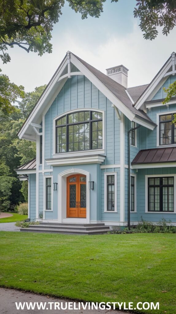 A charming light blue house with a gable roof, incorporating natural wood accents around the arched entrance and large, multi-paned windows.