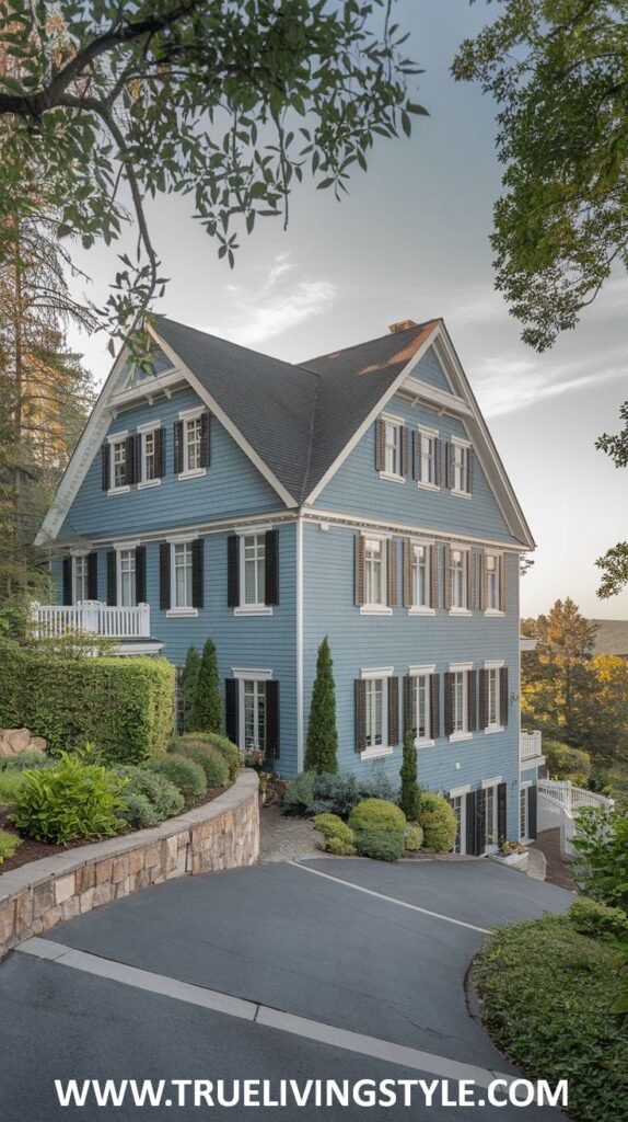 A three-story blue house built on a hillside, featuring numerous windows on all levels and surrounded by stone walls and varied greenery.