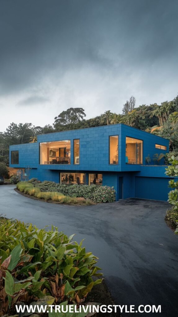 A modern home painted in a monochromatic dark blue, featuring a flat roof, generous window placements, and dark landscaping.