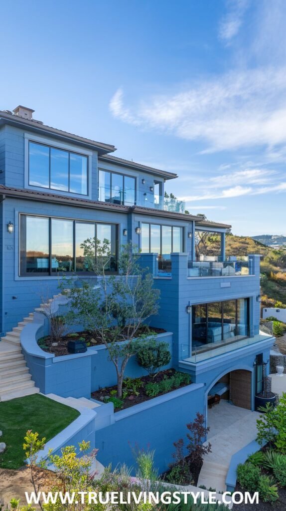 A multi-level house painted in a consistent blue hue, built into a sloping landscape with multiple balconies and large windows.