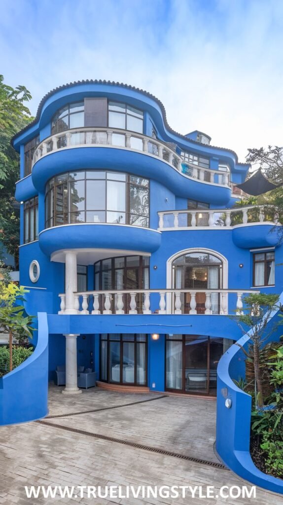 A unique curvilinear house painted in a vibrant blue, featuring multiple balconies with white railings and curved architectural forms.