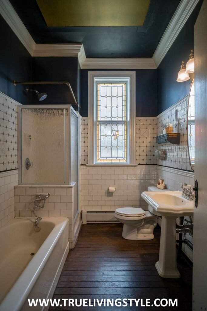 An elegant victorian bathroom with dark blue walls, white tiled lower half, a clawfoot bathtub with a glass shower enclosure, a stained glass window, a pedestal sink, and a toilet.