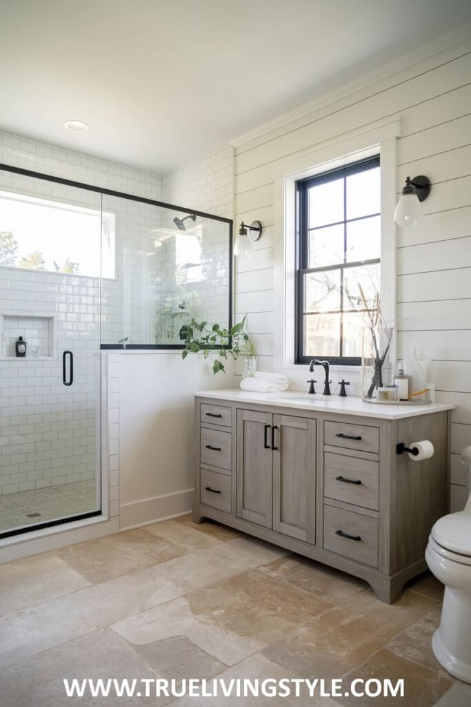 Modern farmhouse bathroom with a glass-enclosed walk-in shower featuring white subway tiles, a gray double vanity with a light countertop, a toilet, light stone-look tiled flooring, and white shiplap walls.