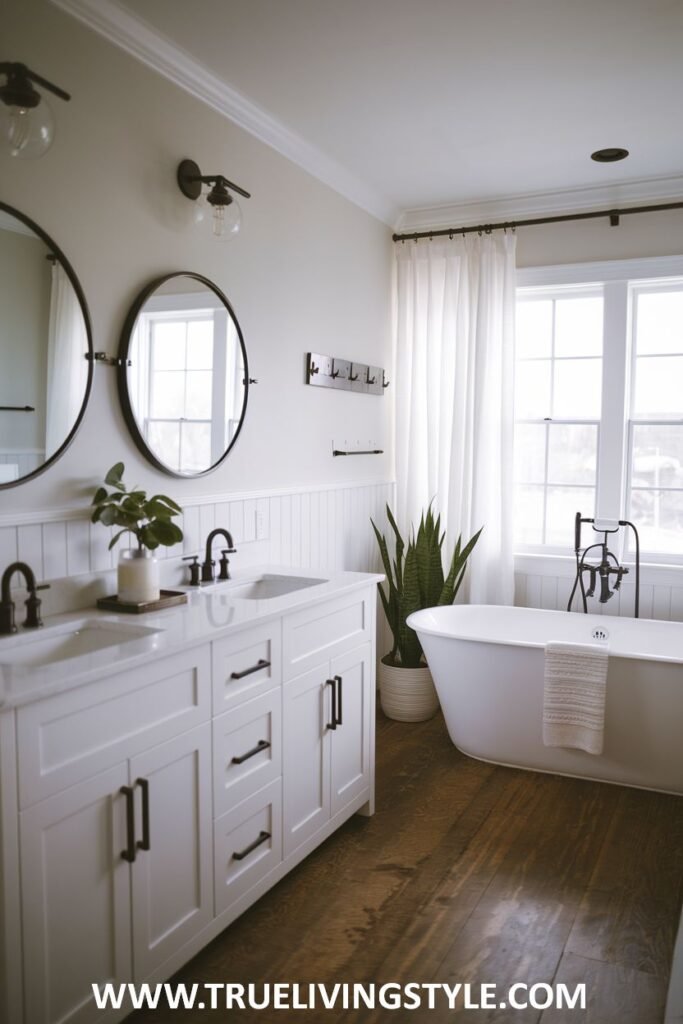 Modern farmhouse bathroom with a white freestanding soaking tub, a white double vanity with black hardware and a white countertop, two round mirrors, a toilet, white shiplap walls, a window with white curtains, and wood plank flooring.