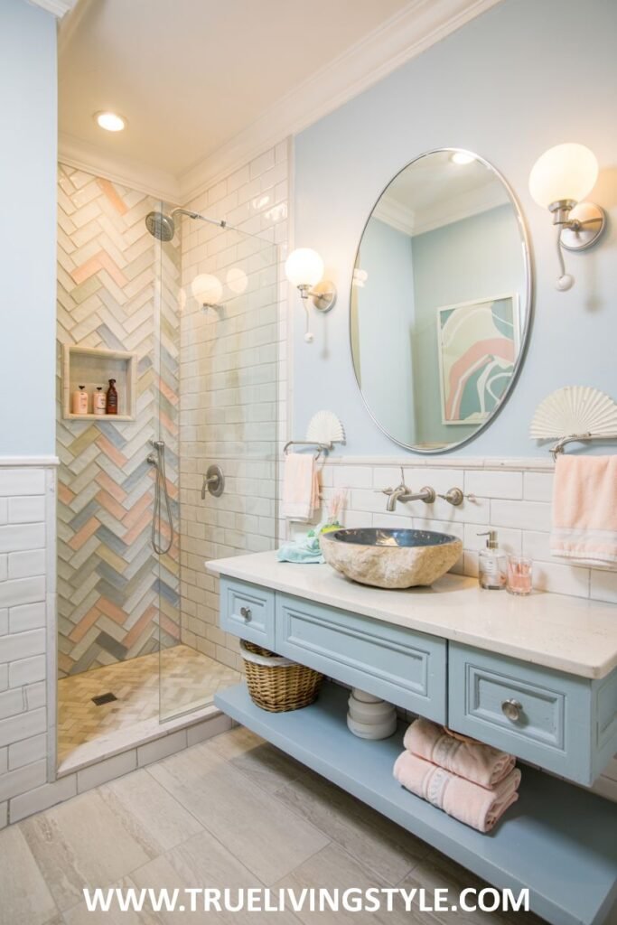 A pastel blue and white bathroom includes a glass-enclosed shower with patterned tiles, a light blue vanity with a unique stone sink, and a round mirror. This is a view of a pastel bathroom.