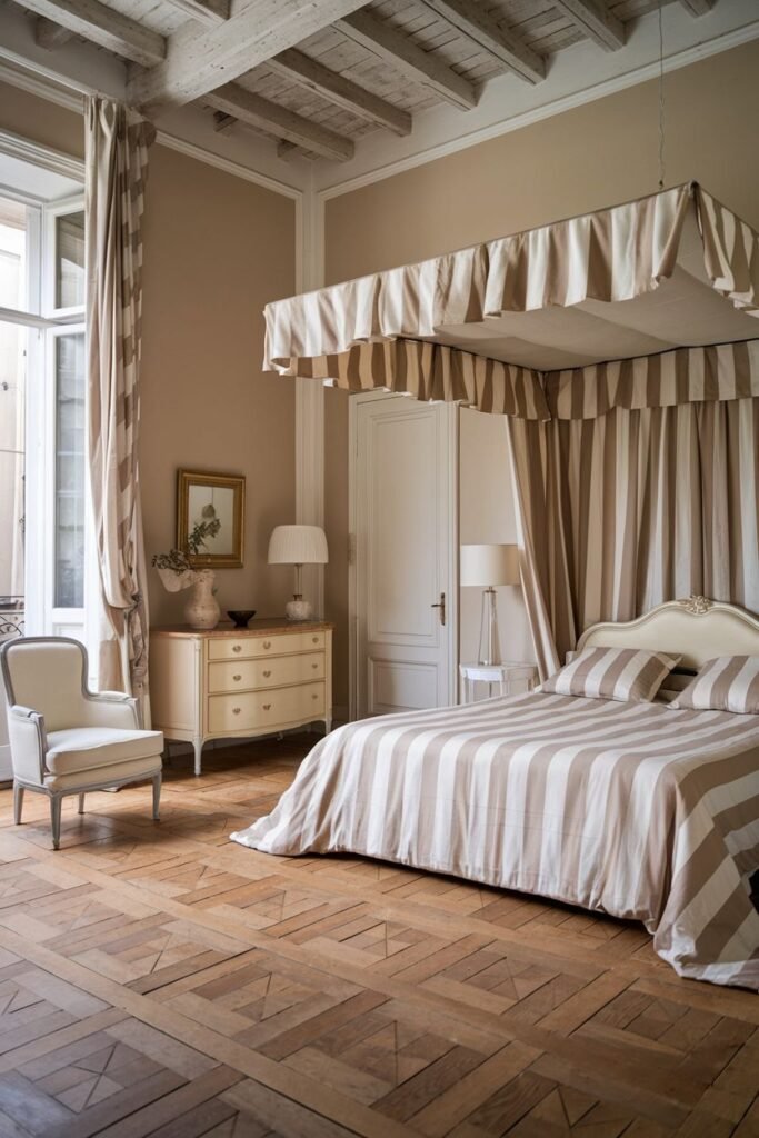 A rustic yet elegant comfortable french bedroom with exposed wooden ceiling beams and large windows. The room features a four-poster bed with striped canopy and bedding, and a dresser.